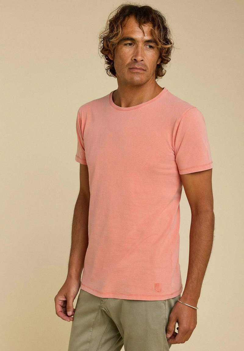 T-shirt à manches courtes, col rond en coton rose clair, avec une texture subtile et un petit logo près de l'ourlet.