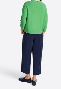 Pull vert texturé à manches trois quarts, associé à un pantalon large bleu marine et des ballerines noires, vu de dos.
