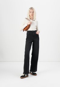 Black high-waisted jeans with a straight leg design, paired with a cream ribbed long-sleeve top and black sneakers with white accents.