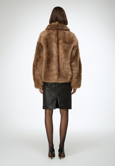 Bruine jas van nepbont met een zachte structuur, brede mouwen en een kraag, gecombineerd met een zwarte leren rok met een split aan de achterkant.