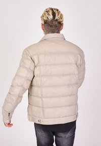 Beige pufferjakke med quiltet design, trykknaplukning og blød tekstur. Jakken har en simpel krave og lange ærmer.