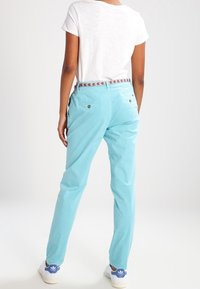 Osoba ubrana w białą koszulkę, jasnoniebieskie spodnie z zapiętymi tylnymi kieszeniami, wzorzystym paskiem oraz białe trampki z niebieskimi akcentami.