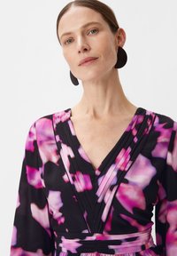 Blumenkleid mit schwarzem Grundton und abstrakten Mustern in Rosa und Lila, V-Ausschnitt, plissierten Akzenten und langen Ärmeln.