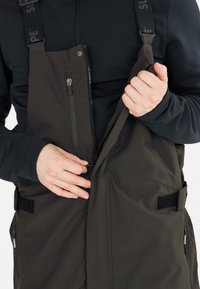 Mörkgröna overaller med justerbara remmar, frontdragkedjor och sidofickor. Tyget verkar vara vattenavvisande med en strukturerad yta.