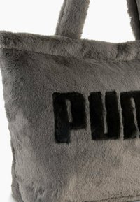 Borsa tote in finta pelliccia grigia con logo "PUMA" ricamato in nero. Presenta due manici robusti e una superficie morbida e testurizzata. Forma rettangolare.