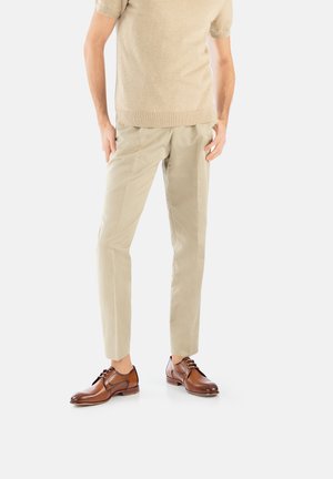 Pull à manches courtes beige, pantalon beige clair et chaussures habillées en cuir marron avec lacets. Les chaussures présentent une finition polie et des pointes arrondies.