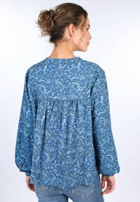 Blaue Bluse mit Blumenmuster, langen Ärmeln, runder Ausschnitt und gerafftem Rückendetail. Der Stoff hat eine weiche Textur mit Variationen in blauen Farbtönen.