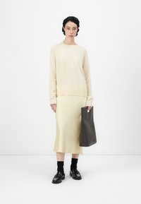 Light beige sweater, cream midi skirt, black loafers, and textured black tote bag. Simple design, soft textures, and neutral colors.