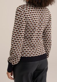 Stickad tröja med ett geometriskt mönster i brunt, vitt och svart, med en ribbad svart fåll och ballongsärmar.