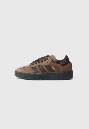 Bruine Adidas Samba sneaker met donkerbruine strepen, bovenwerk van suède en mesh, zwarte gestructureerde zool en gouden "SAMBA" tekst aan de zijkant.
