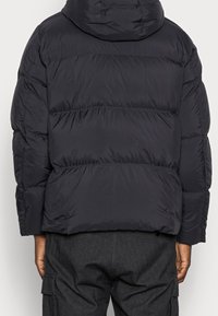 Czarna kurtka puchowa z kapturem, z pikowanym wzorem i wieloma poziomymi sekcjami, wykonana z gładkiego, błyszczącego materiału.