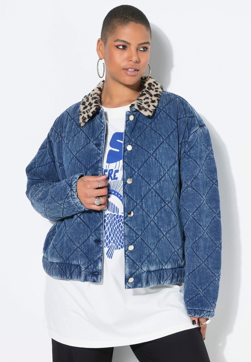 Pikowana kurtka dżinsowa z kołnierzem w panterkę, ozdobiona srebrnymi zatrzaskami i luźnym krojem. Noszona na białej koszulce z nadrukiem.