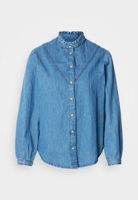 Blå denimskjorte med rysjekrage, knappestolpe foran og lange ermer. Har dekorative sømmer og en lett buet kant nederst.