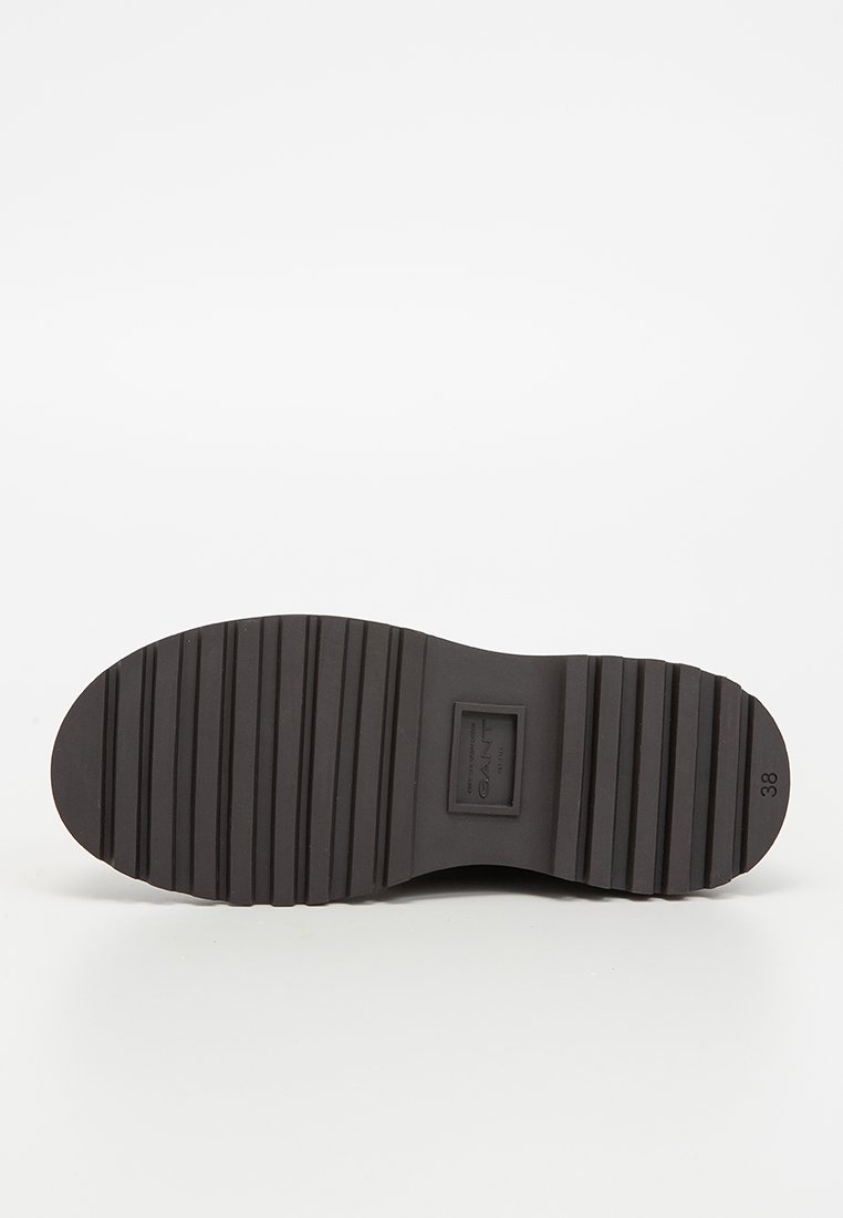 Svart gummisul med en strukturerad yta som har horisontella ribbor. Inkluderar en etikett märkt "GANT" och storlek "38."