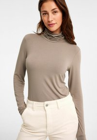 Långärmad polo-top i taupe jersey-tyg, med en rynkad halsringning. Matchas med ribbad krämfärgad kordflöjtbyxor.