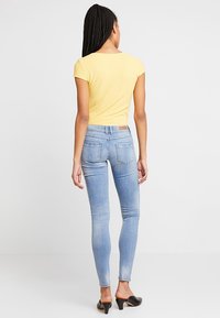 Ljusgul ribbad topp, åtsittande blå skinny jeans med bakfickor och svarta klackskor. Slät textur, avslappnad design och skräddarsydd passform.