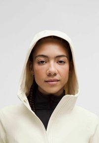 White hooded jacket with a smooth texture, layered over a black high-collared top. The design features a modern, clean-cut silhouette.