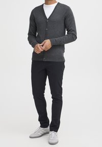 Mörkgrå kofta med v-ringning, knappstängning, ribbade muddar och fåll. Bärs över en vit skjorta tillsammans med marinblå byxor och grå sneakers.