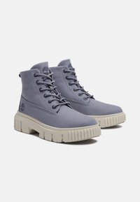 Botines con cordones en tela de canvas gris claro con un acabado texturizado y suela de goma gruesa en color crema contrastante. Presenta un logotipo en el lateral.