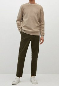 Pull en tricot beige clair avec un col rond, associé à un pantalon olive slim-fit et des baskets blanches. Design simple et moderne.