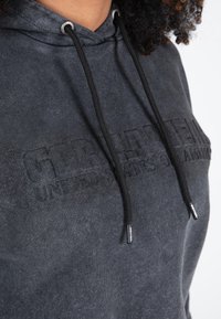 Donkergrijze hoodie met verstelbare zwarte trekkoorden, met een reliëf logo detail aan de voorkant. Zachte stof met een ontspannen pasvorm.