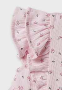 Tissu rose avec de petits motifs floraux et des feuilles vertes, bordé de volants et en textile structuré, mettant en avant un design doux et léger.