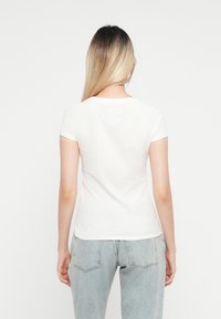 Hvit kortermet t-skjorte med rund hals, myk tekstur og en tettsittende design, kombinert med lyseblå høyt liv jeans.