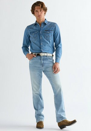 Vaaleansininen farkkupaita, jossa länsityyliset ompeleet ja kaksi rintataskua, yhdistettynä haalistuneisiin sinisiin farkkuihin ja ruskeisiin cowboy-saappaisiin.