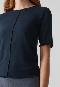 Navyblauw kortmouwen top van zachte stof, met een ronde halslijn en gekartelde zoomdetails. Minimalistisch ontwerp met een centrale naad.