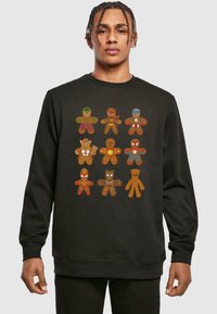Felpa nera con personaggi di pan di zenzero in stile cartone animato, ciascuno vestito con diversi costumi da supereroe. Il design include colori multipli e dettagli ricercati.