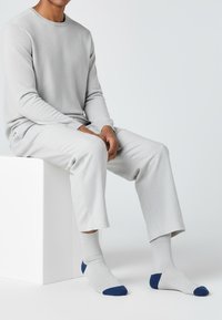 Lysegrå striktrøje med rund halsudskæring kombineret med matchende grå bukser, suppleret med grå sokker med marineblå accenter.