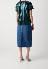 Teal, metallisk kortärmad topp med ett nyckelhål i ryggen, tillsammans med en midikjol i denim, med rak skärning och bakfickor.