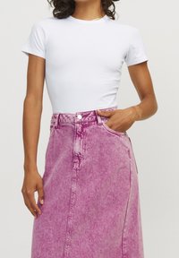 Vit t-shirt med kort ärm som passar nära kroppen, kombinerad med en höga midja rosa denimkjol med knäppning och subtila urtvättningsdetaljer.