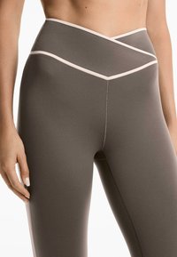 Hochtaillierte Leggings aus einem dunkelgrauen Stoff mit glatter Textur. Verfügt über eine kontrastierende, hellrosa Umrandung und diagonale Nähte.