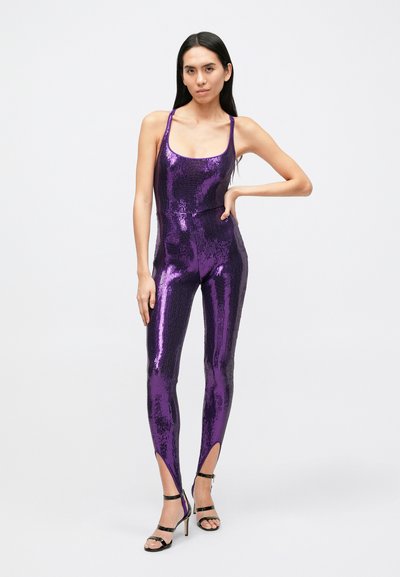Combinaison violette à sequins avec une coupe ajustée, des bretelles spaghetti et des découpes aux chevilles. Caractérisée par une texture brillante et une silhouette moulante.