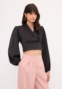 Schwarze Kurzbluse mit puffartigen langen Ärmeln und tiefem V-Ausschnitt, verziert mit drei dekorativen goldenen Knöpfen auf der Vorderseite und einer glatten Textur.