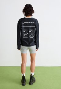 Juodas ilgomis rankovėmis marškinėliai su baltais akcentais ir numeriu 23 ant nugaros, derinami su pilkais šortais ir juodais platforminiais batais.