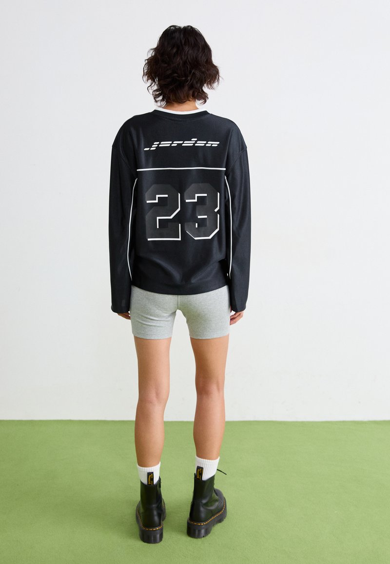 T-shirt noir à manches longues avec des accents blancs et le numéro 23 dans le dos, associé à un short gris et des bottes plateformes noires.