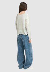 Hellgrauer langärmeliger Pullover mit weitem Ausschnitt, kombiniert mit locker sitzenden blauen Denim-Jeans mit hinteren Taschen und einem ausgewaschenen Textur.