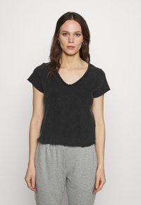 Melna, īsām piedurknēm t-kreklu ar V veida kakla izgriezumu, iezīmējot neapstrādātu apakšmalu un brīvu piegriezumu, parādīts uz vienkārša balta fona.