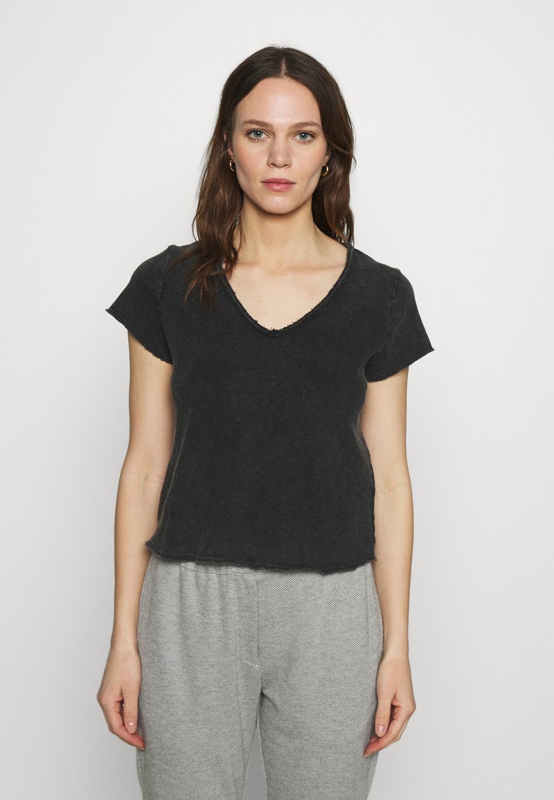 Melna, īsām piedurknēm t-kreklu ar V veida kakla izgriezumu, iezīmējot neapstrādātu apakšmalu un brīvu piegriezumu, parādīts uz vienkārša balta fona.