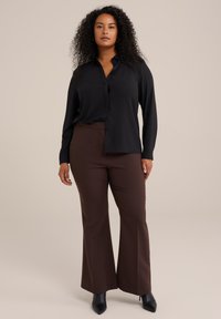 Blusa nera a maniche lunghe con bottoni frontali, abbinata a pantaloni larghi marroni. Tessuto testurizzato. Stivaletti neri con tacco. Design semplice.