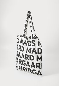 Borsa tote in tessuto bianco con testo nero audace, stampata con le parole "MADS NØRGAARD". Ha manici lunghi e decorati per un facile trasporto.