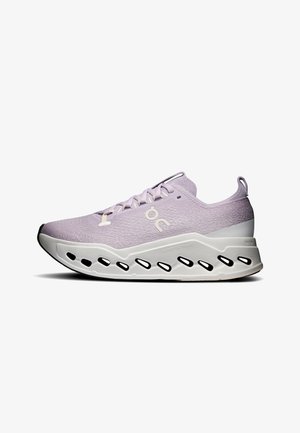 Chaussure de sport violet clair avec semelle blanche, présentant des découpes ovales noires et une languette au talon, logo latéral visible sur la tige en maille.