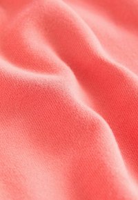 Zbliżenie na koralowy materiał, prezentujący gładką teksturę z delikatnym wzorem dżersejowym, lekko pomarszczony, ukazujący bogaty i intensywny odcień.