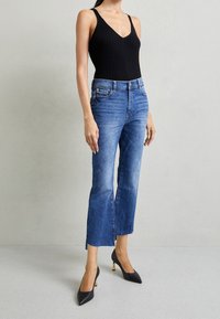 Body negro acanalado con escote en V profundo, combinado con jeans de talle alto de color azul claro con dobladillo deshilachado y tacones negros puntiagudos con detalles dorados.