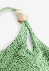 Borsa in tessuto verde, con texture e design arricciato, dotata di due perle di marmo chiare all'incrocio delle cinghie.