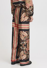 Zwarte patroonbroek met een paisley-ontwerp in goud, rood en crème. Het ontwerp omvat horizontale strepen en een trekkoord in de taille.