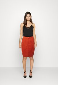 Camisola preta com rendas, saia lápis de veludo cotelê vermelha, com frente de botões e bolsos, combinada com sapatos de salto agudo pretos.