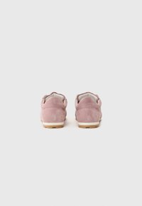 Chaussures en suède rose pâle avec une texture douce, un design à profil bas et des semelles en caoutchouc blanche. Elles présentent un talon arrondi et des détails de coutures minimaux.